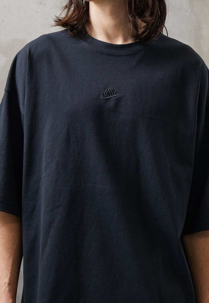 Černé bavlněné tričko s krátkými rukávy a kulatým výstřihem, s vyšívaným logem Nike na hrudi. Jednoduchý, neformální design.