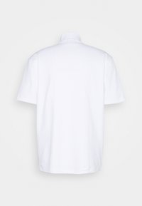 Polo à manches courtes blanches unies, vu de dos, avec un col, sur un fond gris clair.