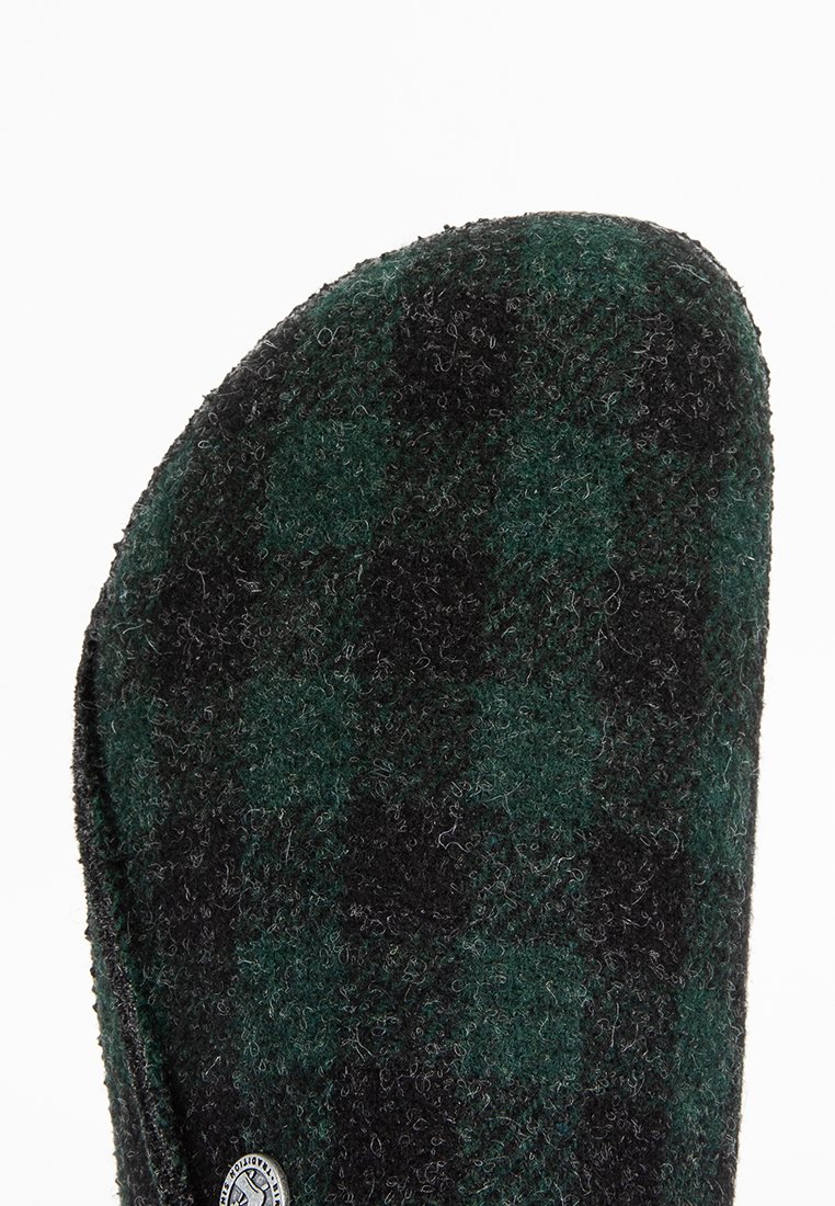 Wollene Hausschuhe mit einem schwarz-grünen Karomuster, runder Form und einer strukturierten Oberfläche sowie einem kleinen Logo an der Seite.