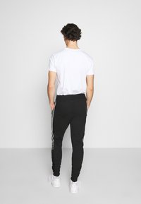 Zwarte joggers met witte zijstrepen, tapersnit, elastische tailleband en ribgebreide boorden. Gemaakt in combinatie met een eenvoudig wit T-shirt.