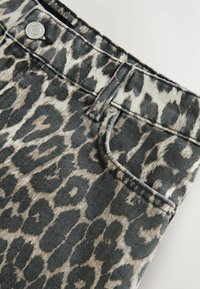 Jean en denim imprimé léopard avec une base beige clair et des taches marron foncé, dotés de détails en métal argenté et d'une poche avant.