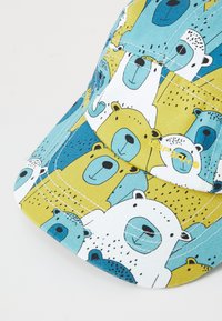 Casquette présentant un motif de bear coloré en bleu, jaune et blanc, fabriquée en tissu avec une surface texturée et des détails de couture contrastants.