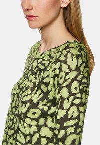 Grüner Leopardenmuster-Sweatshirt mit Rundhalsausschnitt, kontrastierenden Nähten und weichem Material. Der Stoff wirkt leicht und lässig.