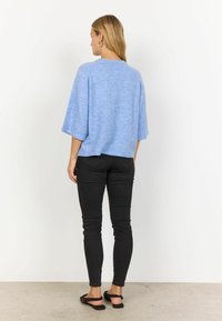 Blaues Stricktop mit lockerer Passform, tief sitzenden Schultern und kurzen Ärmeln, kombiniert mit schwarzen Slim-Fit-Jeans und schwarzen Sandalen.