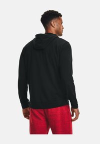 Sort hættetrøje med snøre i hætten, der har en glat tekstur. Bæres med røde melerede shorts, der fremhæver et afslappet fit og en uformel stil.