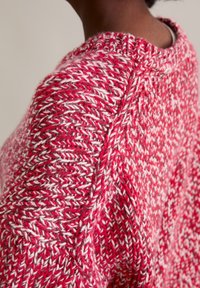 Rot-weißer gemusterter Strickpullover mit strukturierter Oberfläche und geripptem Ausschnitt, der einen lockeren Schnitt und sichtbare Nähte aufweist.