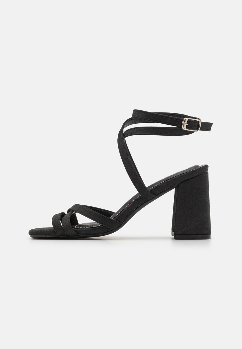 Svart strappy sandal med blokkheel, laget av mykt semsket skinn, med kryssremmer og spennefeste rundt ankelen.