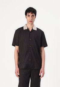 Camicetta a maniche corte a righe nere con colletto beige, caratterizzata da una chiusura con bottoni e una vestibilità rilassata. Adatta per un abbigliamento casual.