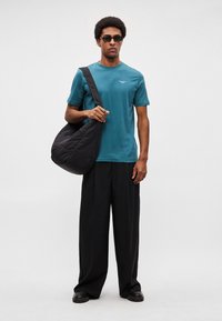 Tricou din bumbac verde-albăstrui, pantaloni negri supradimensionați, geantă neagră crossbody și ochelari de soare negri. Design simplu, minimalist, fără modele.