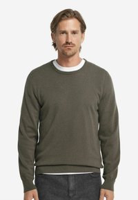 Olivgrön stickad tröja med långa ärmar, rund halsringning och ribbade muddar och nederkant. Lager på en vit T-shirt.