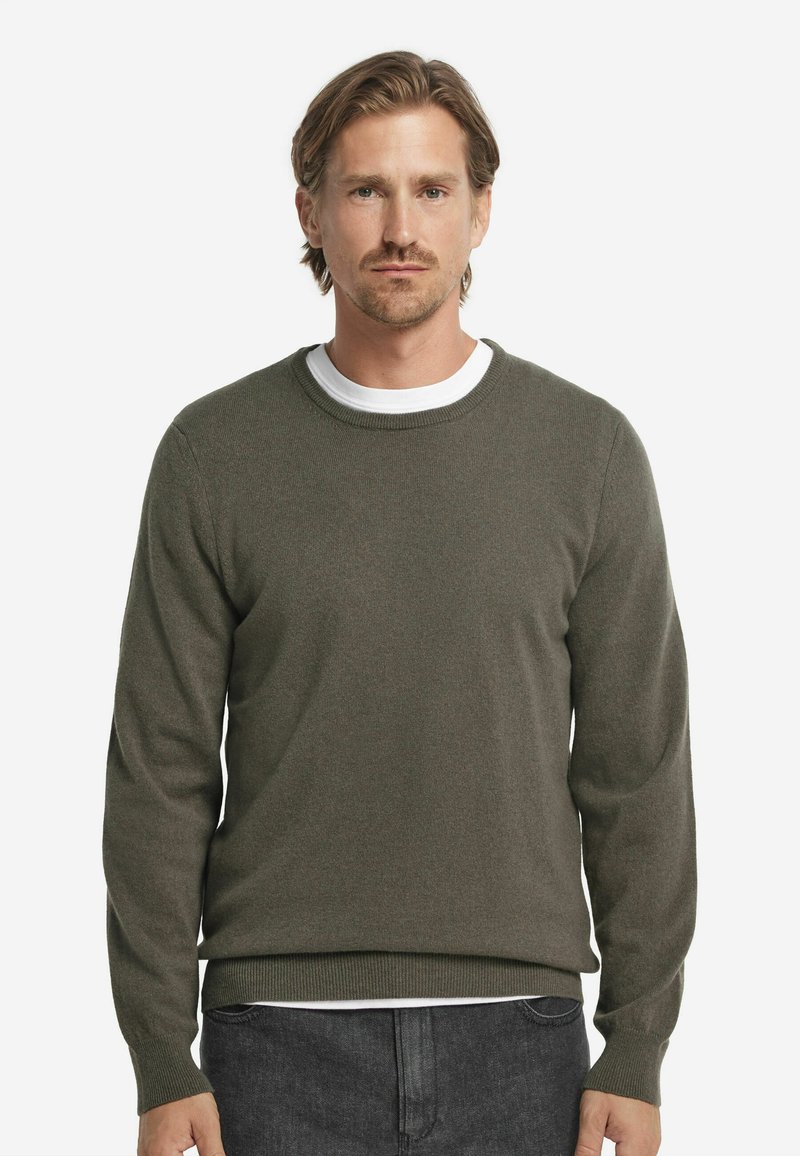 Olivgrön stickad tröja med långa ärmar, rund halsringning och ribbade muddar och nederkant. Lager på en vit T-shirt.