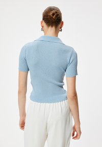 Ljust blå randig kortärmad polo med krage, med en figurnära silhuett och en vågig nederkant.