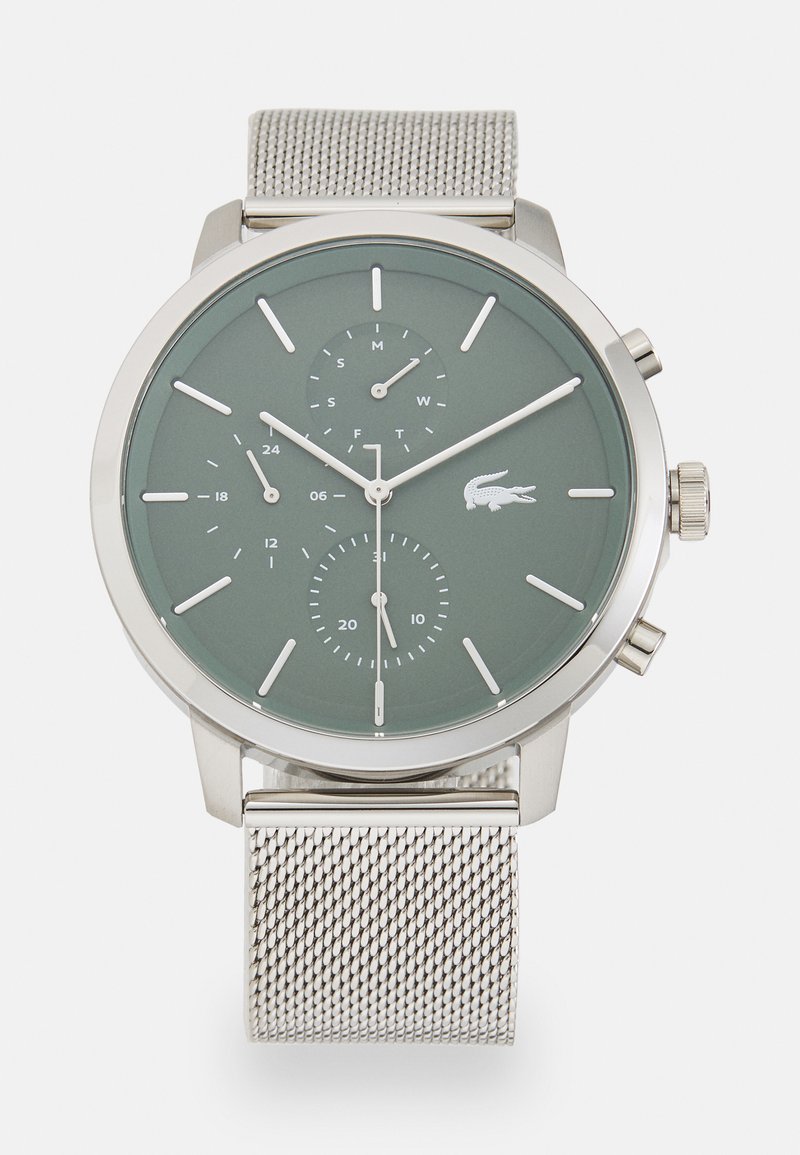 Silver metal watch with a green dial, featuring two sub-dials and white hour markers. It has a mesh strap and Lacoste logo at the 6 o'clock position.
