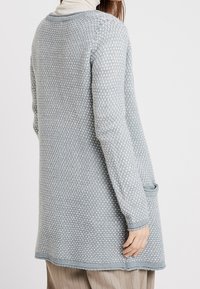 Ljusgrå cardigan med ett texturerat stickmönster, med en lång design, en ficka på höger sida och ribbade manschetter.