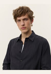 Black button-up shirt with a textured pattern, long sleeves, and a classic collar. Features front placket with buttons and minimalistic design.