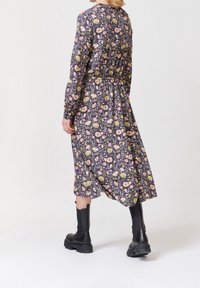 Robe à motif floral avec manches longues, taille froncée et ourlet jusqu'aux chevilles. Tissu arborant des couleurs vives sur un fond sombre. Bottes noires.