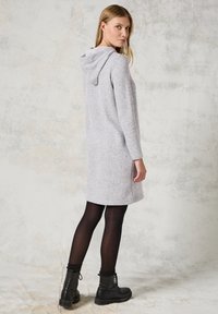 Grå stickad klänning med huva, långa ärmar och sidoklipper. Bärs med svarta tights och snörkängor. Texturerad tyg, figurvänlig stil.