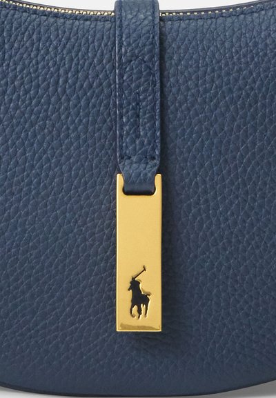 Meripäällysteinen tummansininen nahkalaukku, jossa on teksturoitu pinta. Laukussa on kultainen suorakulmainen varuste, jossa on ratsastajan siluetti. Vetoketjukiinnitys.