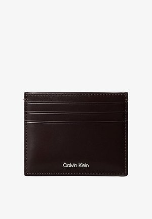 Porte-cartes en cuir marron foncé avec quatre emplacements pour cartes et logo Calvin Klein argenté dans le coin inférieur droit.
