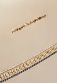 Borsa a tracolla in pelle beige con logo color oro, scomparto con cerniera a denti metallici e superficie liscia e strutturata.