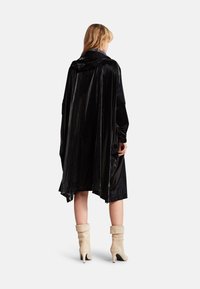 Černý, lesklý kabát s kapucí, s volným střihem a dlouhými rukávy; doplněný krémovými vysokými, volnými kotníkovými botami.