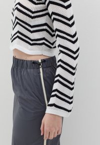 Maglione lavorato all'uncinetto a righe bianche e nere con maniche lunghe, abbinato a pantaloni grigi con vita elasticizzata e zip laterale.