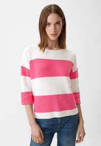 Roze en witte gestreepte gebreide trui met driekwartmouwen, textuurstof en een brede ronde hals. Gepaarde met blauwe spijkerbroeken.