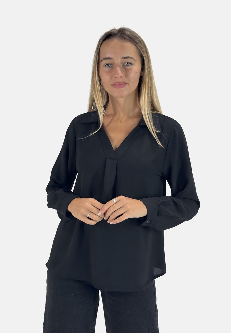 Blusa nera a maniche lunghe con scollo a V, dettaglio con piega frontale e polsini con bottone. Tessuto liscio e vestibilità morbida. Abbinata a pantaloni scuri.