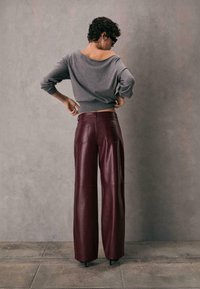 Grå off-shoulder sweater med lange ærmer, parret med højtaljede, vidde bukser i burgunderrød læder med baglommer og glat tekstur.