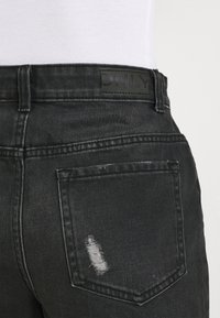 Pantalones vaqueros de mezclilla negra con un parche desgastado en el bolsillo trasero, etiqueta negra con la inscripción "ONLY" en relieve, corte recto y cintura estándar.