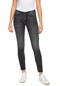 Jeans de denim negro ajustados con cintura de altura media, diseño de cinco bolsillos, ligero desgaste y detalles de costura en los bolsillos. Llevados con zapatillas blancas.