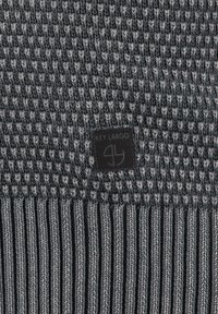 Beanie grigia in maglia con un motivo testurizzato e fondo a coste. Presenta una patch logo in pelle nera. Materiale morbido e caldo.
