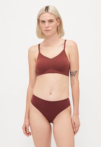 Bralette sem fios burgundy com um delicado acabamento de renda, alças ajustáveis e roupa interior alta combinando com um acabamento liso e sem costuras.
