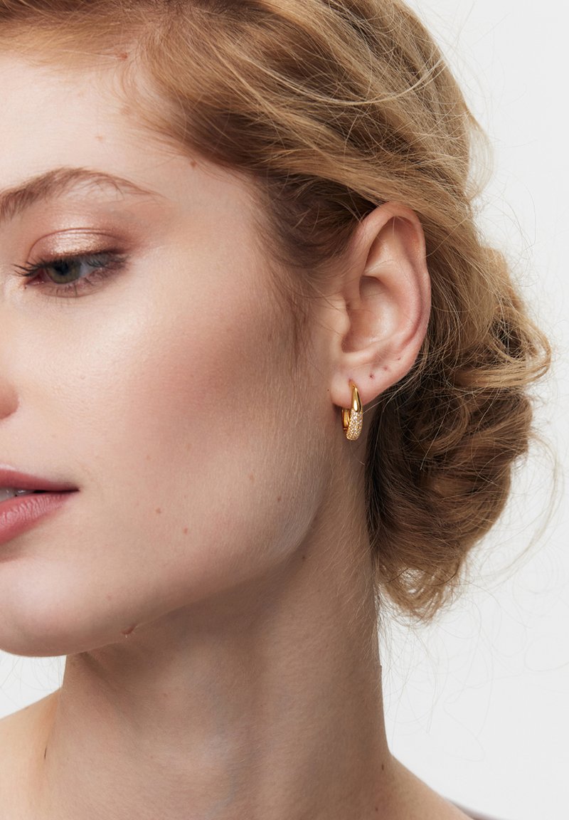 Złote kolczyki koła mają teksturowany wzór z gładkim wykończeniem. Kolczyki mają owalny kształt, co podkreśla elegancję noszącej je osoby.