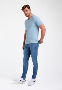 Gaiši zils īsām piedurknēm polo krekls ar teksturētu rakstu, apvienots ar gaiši ziliem šauriem džinsiem un baltiem sporta apaviem ar melnu logotipu.