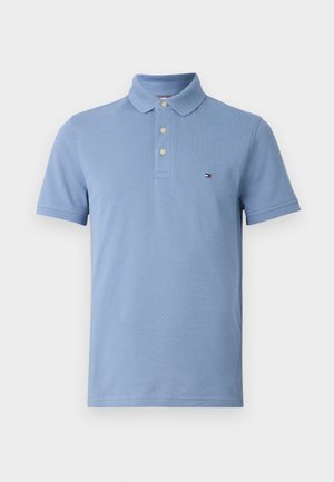 Polo a maniche corte azzurro chiaro con tre bottoni e un piccolo logo a bandiera sul petto sinistro, mostrato su sfondo bianco.