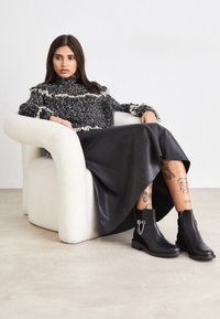 Černé kožené kotníkové boty s řetízkovým detailem, doplněné o černou texturovanou dlouhou sukní a černobílý svetr s tečkovaným vzorem.