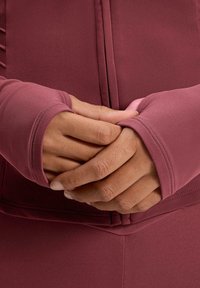 Hosszú ujjú sportos felső mély rózsaszín anyagból, szűkített mandzsettákkal és sima textúrával, középen összefont kezekkel.