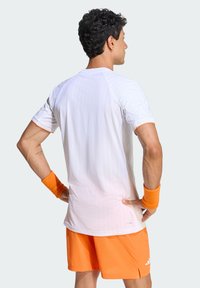 T-shirt de sport blanc à fines rayures verticales, détails orange sur les manches, associé à un short en mesh orange et des bracelets assortis.