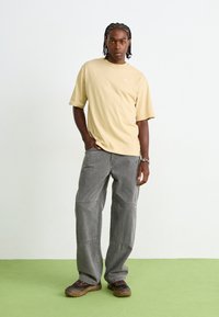 Beige Puma t-shirt met korte mouwen, grijze wijde broek en donkere sneakers met dikke zolen; gladde stof met een casual pasvorm.