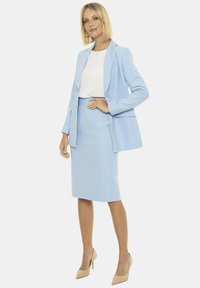 Jasnoniebieska dopasowana marynarka zestawiona z dopasowaną spódnicą ołówkową i białą bluzką. Charakteryzuje się prostymi liniami i dopasowanym krojem. Beżowe szpilki.
