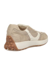 Zapatilla deportiva color beige con parte superior de ante texturizado, paneles de malla y un acento de logo blanco. Suela de goma con clavos hexagonales para mayor tracción.