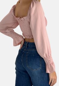 Himmelbluse in zartem Rosa mit langen Puffärmeln, die mit Rüschensaum und einem strukturierten Design gestaltet ist, kombiniert mit hoch taillierten dunkelblauen Jeans.