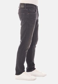 Jeans de mezclilla negra con corte recto, que presentan un diseño de cinco bolsillos y un ligero desgaste, combinados con zapatillas blancas.