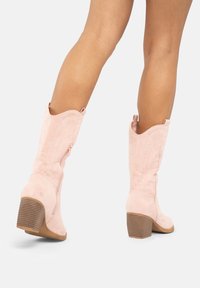 Różowe zamszowe kowbojki z zwężającą się cholewką, skośnym wierzchem i blokowym obcasem, z bocznym zamkiem błyskawicznym oraz teksturowanym obcasem zapewniającym przyczepność.