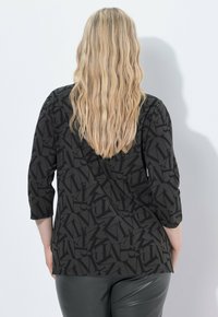 Top nero con un motivo di lettere su tutta la superficie, maniche a trequarti e vestibilità rilassata, abbinato a leggings scuri e lucidi.