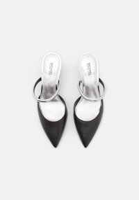 Escarpins slingback en cuir noir avec des pointes effilées, des brides métalliques argentées en accent, et une semelle intérieure lisse et brillante argentée.