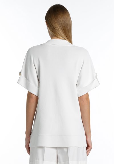 Lockere weiße Bluse mit kurzen Ärmeln, versehen mit Knopfmanschetten. Glatte Textur und verlängerter Saum hinten für eine entspannte Silhouette.