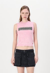 Tettsittende rosa ermeløs topp med en teksturert svart glidelåsdelsdesign over brystet, parret med et svart denimskjørt som har frontlommer.