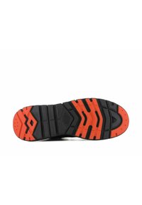 Semelle de chaussure en caoutchouc noire et rouge avec des rainures profondes et des motifs géométriques sur fond blanc, vue du dessous.